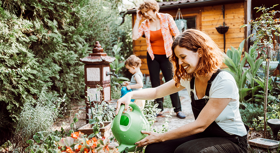 Women waters plants as child and another woman are in backyard