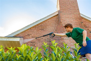 Man sprays landscaping and siding on brick house