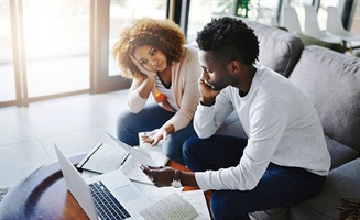man and woman sitting on couch staring at computer, appearing distressed and downtrodden